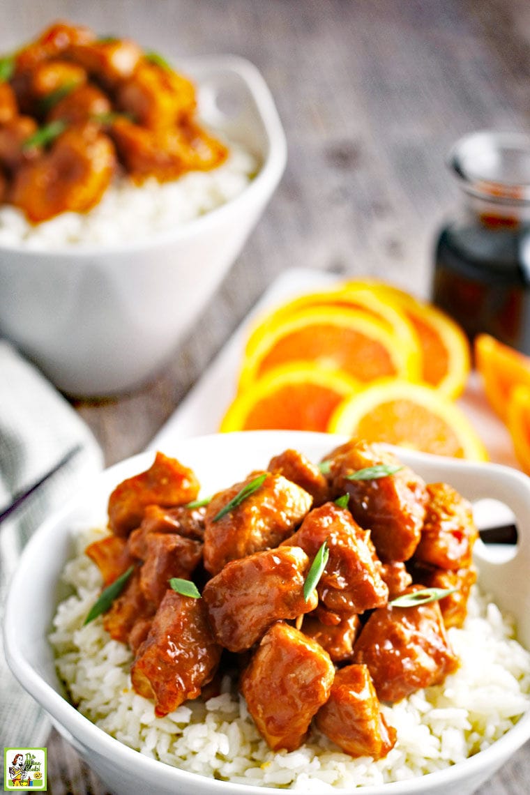 A white bowl of Orange Chicken on white rice with slices of oranges.