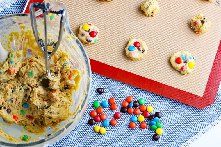 A bowl of M&M Chocolate Chip Cookies dough and a baking sheet of dough balls ready to be baked.