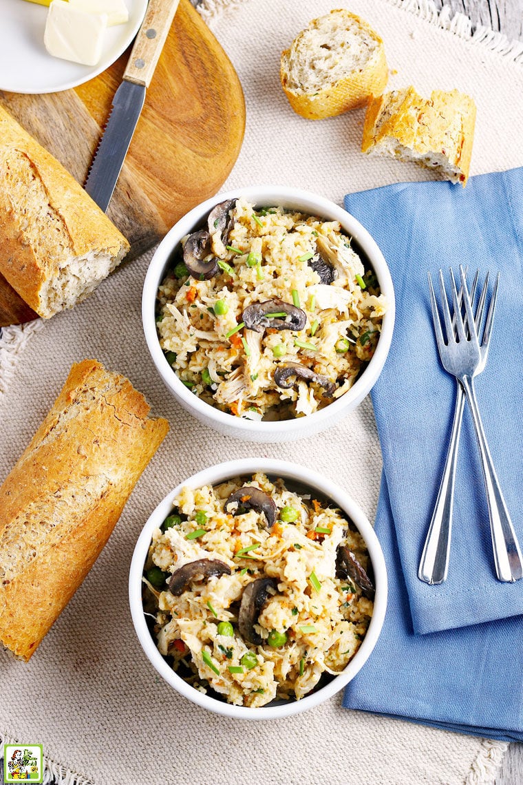 Two white bowls of Instant Pot Chicken and Rice with bread, blue napkins, and forks