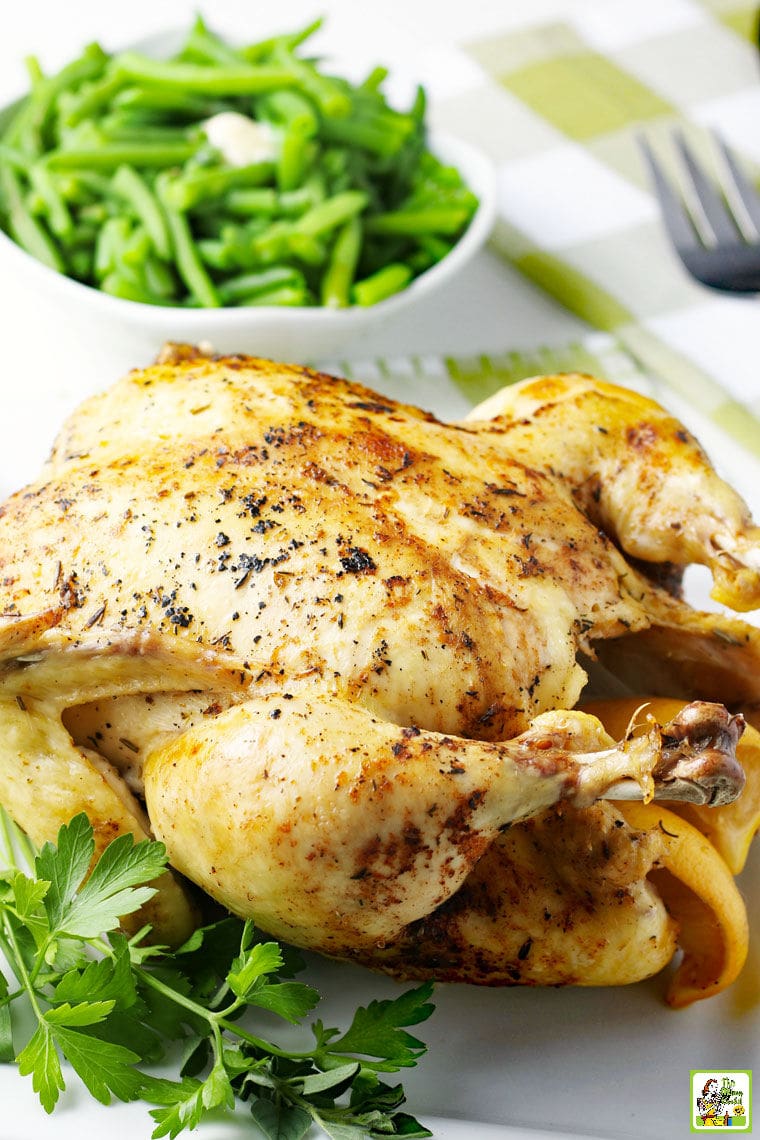 Roasted whole chicken with a bowl of green beans on a green and white checkered tea towel