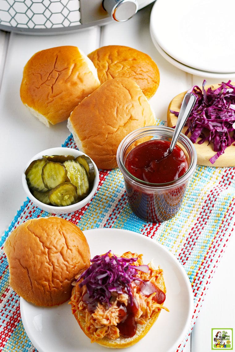 BBQ Chicken Sandwiches with red cabbage, a pot of BBQ sauce, buns, and pickles