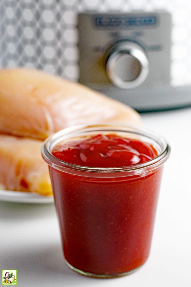 BBQ chicken ingredients - a jar of BBQ sauce, chicken breasts and a crockpot in the background