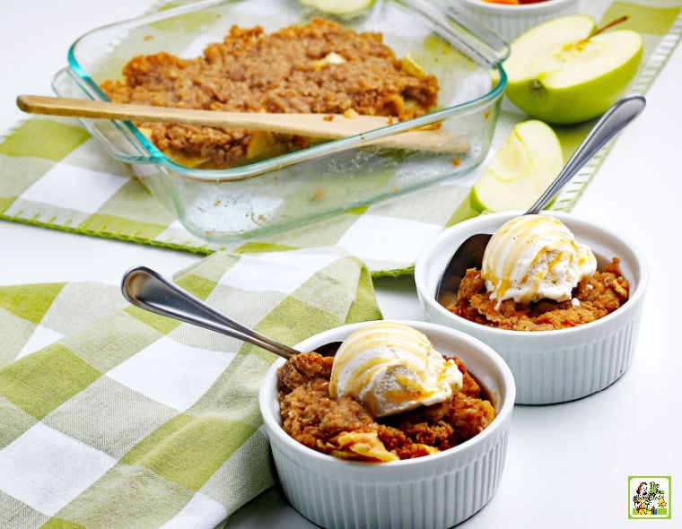 A baking dish of gluten free apple crisp, bowls with scoops of ice cream, slices of apples, and green and white napkins.