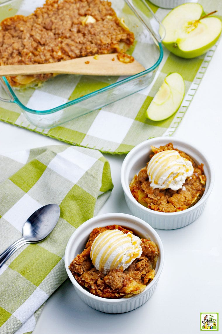 Bowls and a dish of Apple Crisp with spoons and apple slices with green and white napkins.