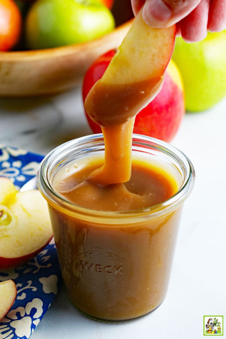 Dipping an apple into a jar of caramel sauce.