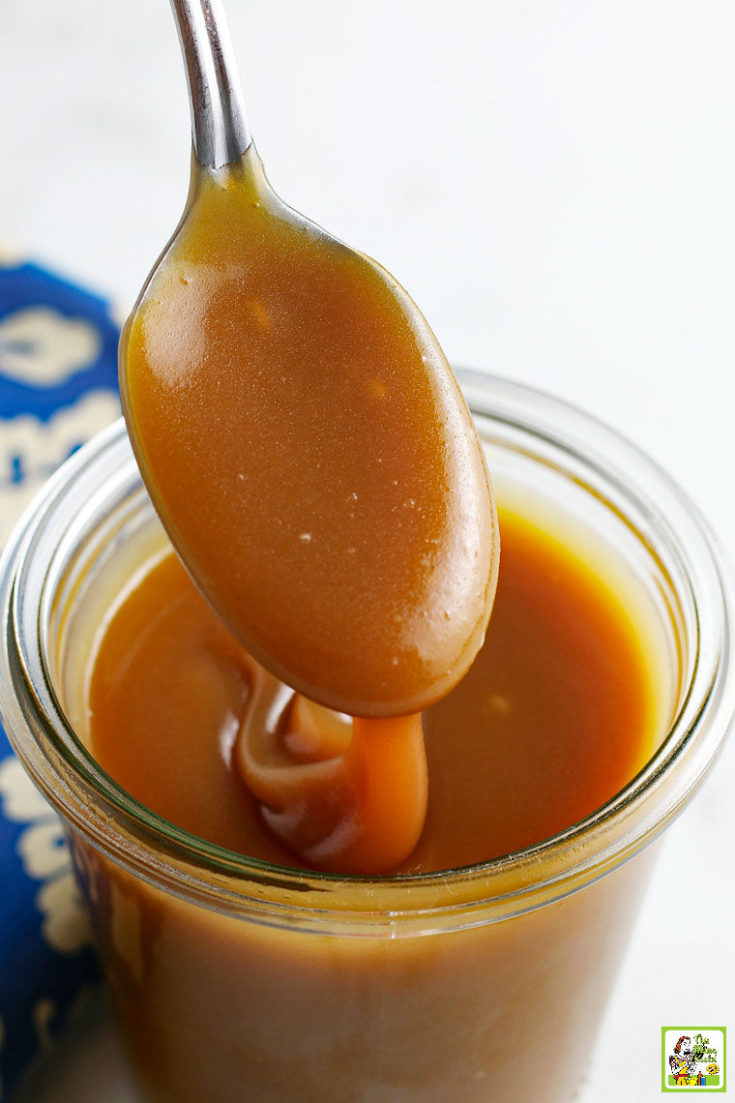 Spooning homemade caramel into a glass jar.