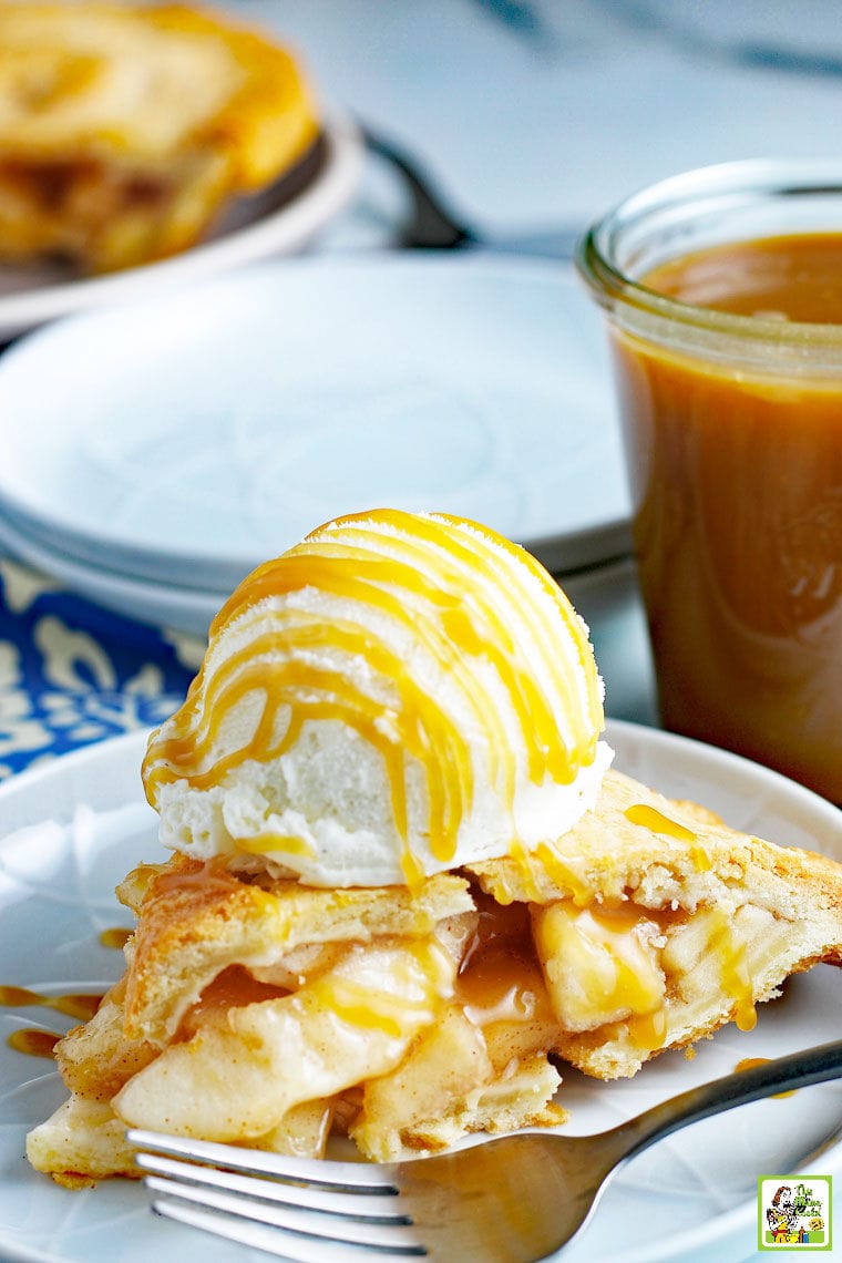 Caramel sauce drizzled on apple pie with a scoop of vanilla ice cream on a white plate with a fork and a jar of caramel sauce.
