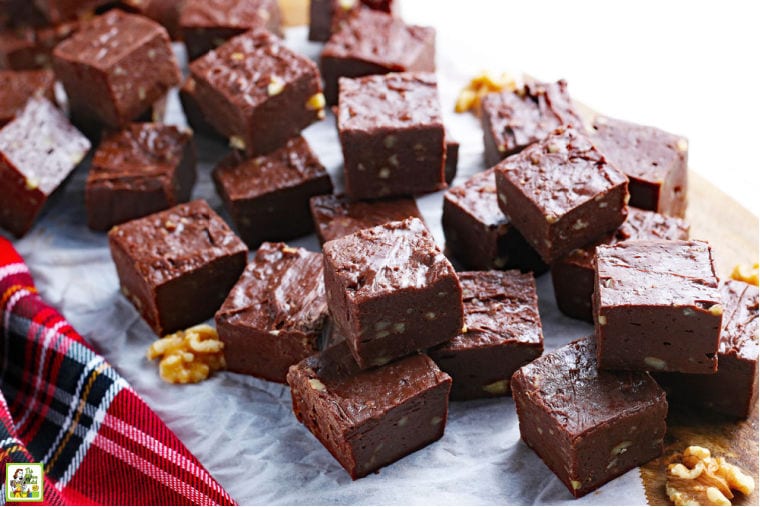 Squares of the best easy fudge recipe ever on parchment paper and a wooden cutting board with walnuts.