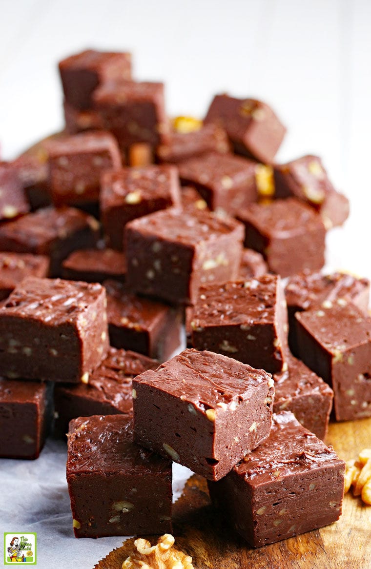 Stacks of homemade fudge with nuts on parchment paper and a wooden cutting board.