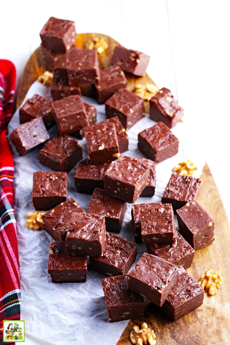 Pieces of easy chocolate fudge on a wooden cutting board with white parchment paper and a plaid napkin.