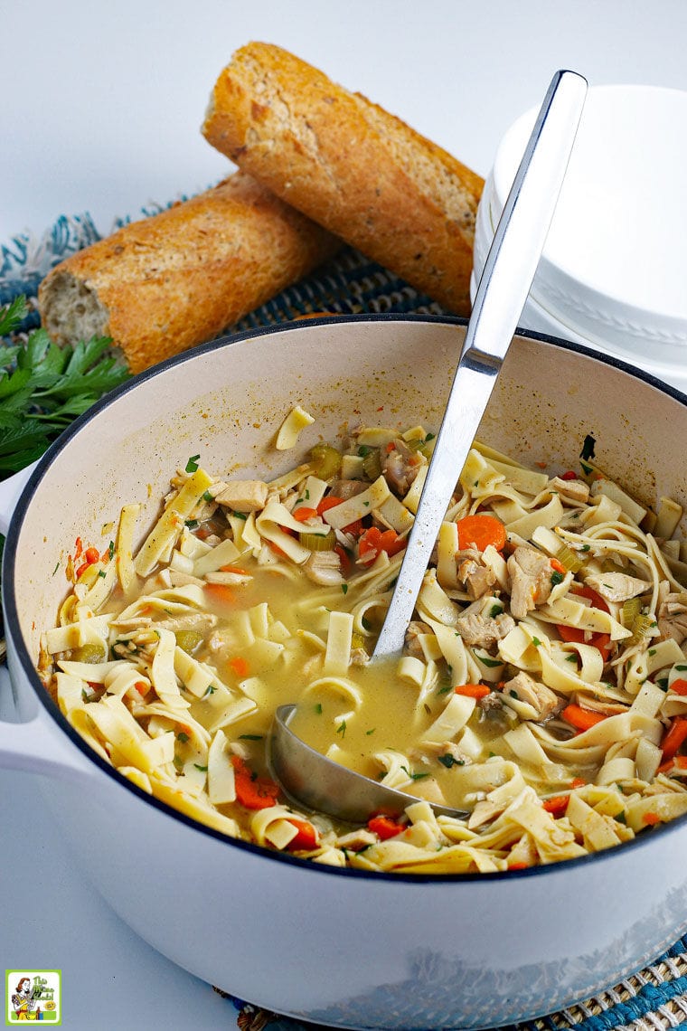 A pot of Leftover Turkey Soup with egg noodles with a ladle and bread.