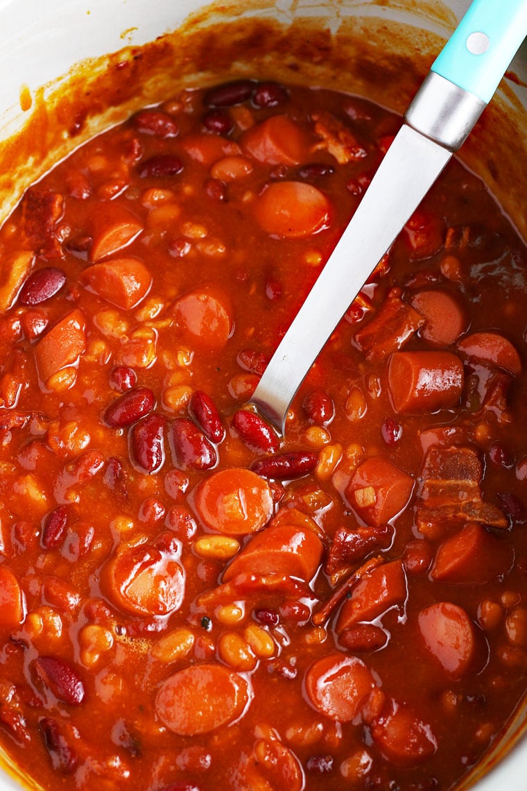 Orverhead shot of a serving spoon in a large crock pot of slow cooker baked beans.