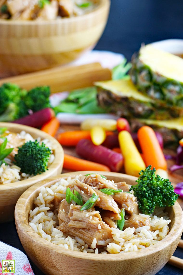 Serving bowls of teriyaki chicken with rice and broccoli with vegetables in the background.