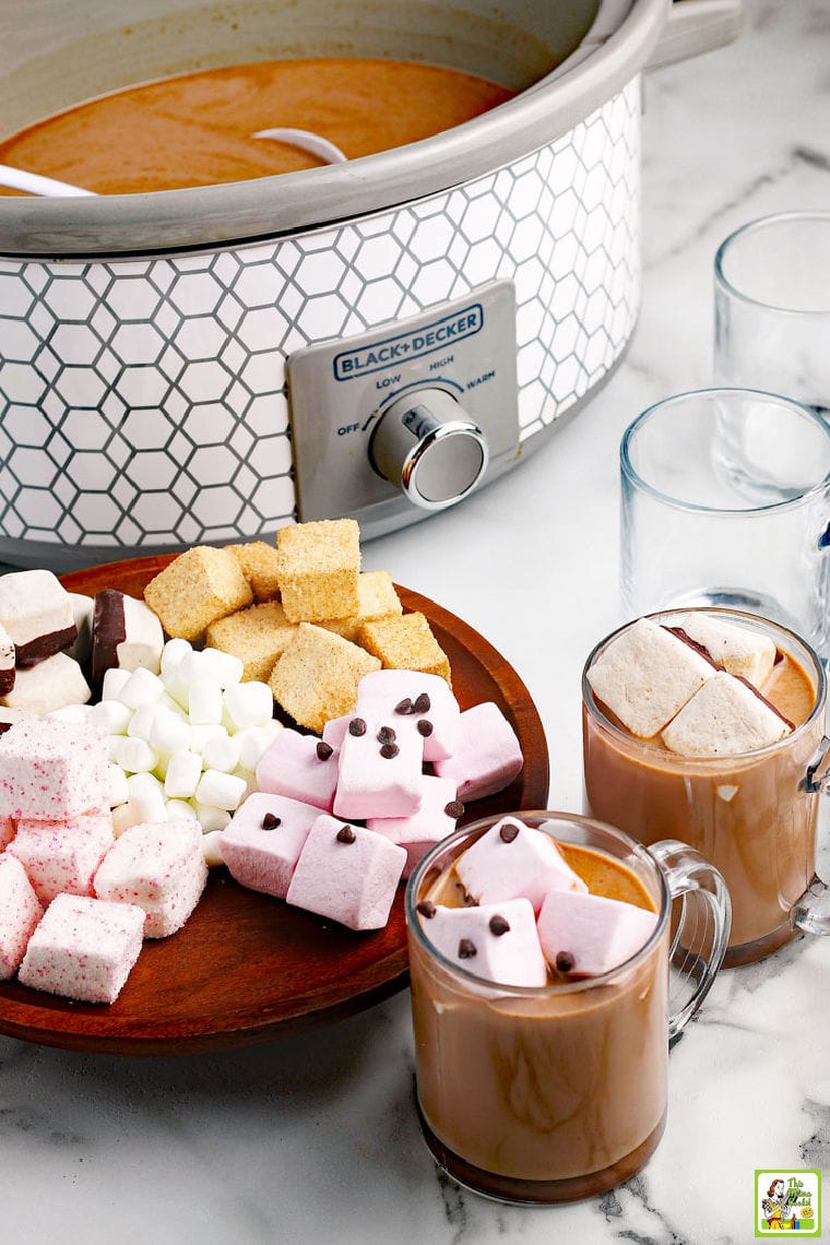 Slow cooker hot chocolate served in glass mugs with colorful marshmallows and chocolate chips.