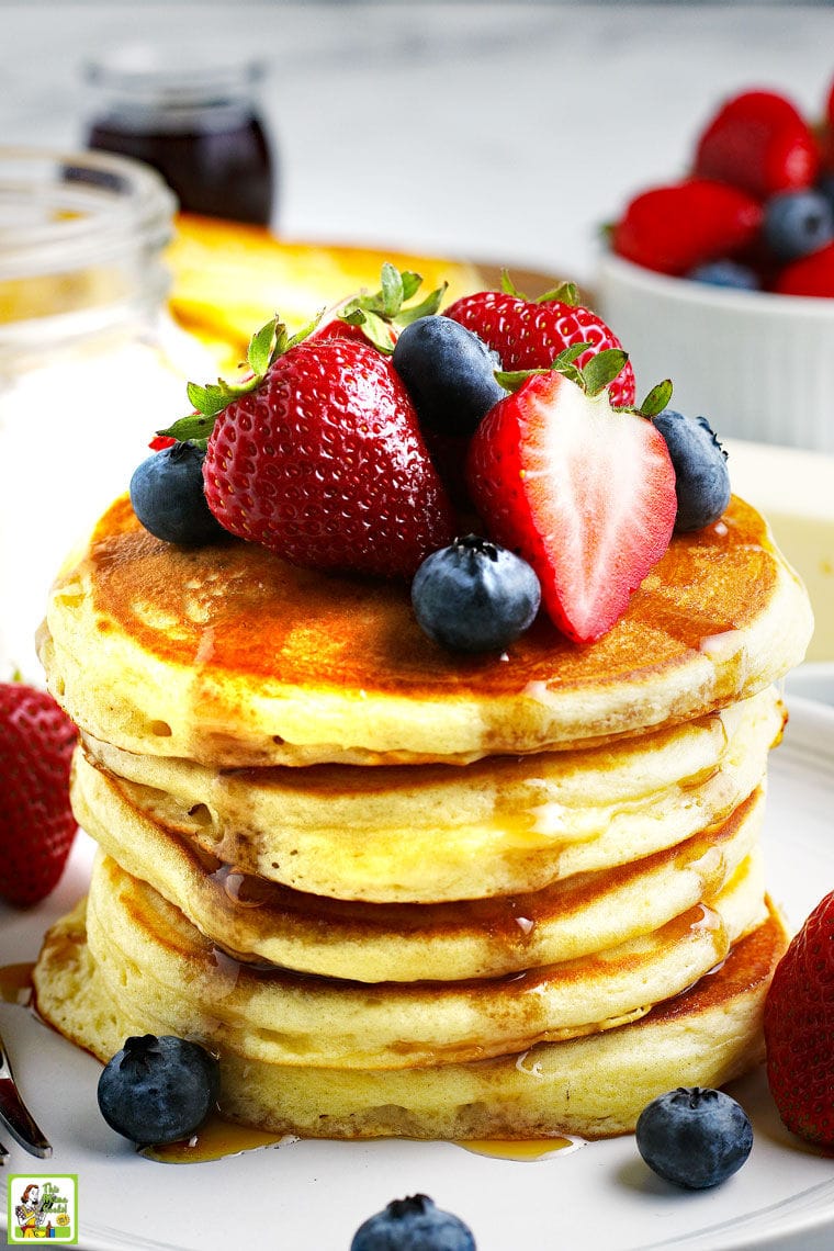 Closeup of a stack of pancakes with fruit and drizzles of maple syrup.