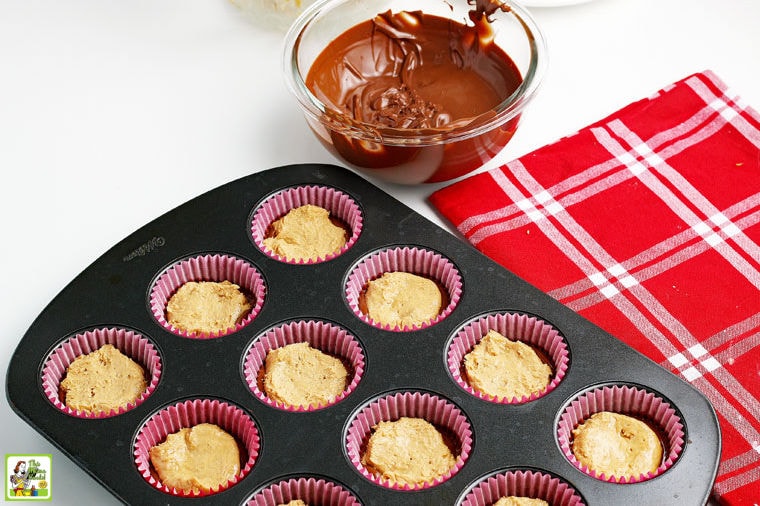 Adding the peanut butter mixture to the melted chocolate layer in the paper lined prepared muffin tins with a red and white tea towel.