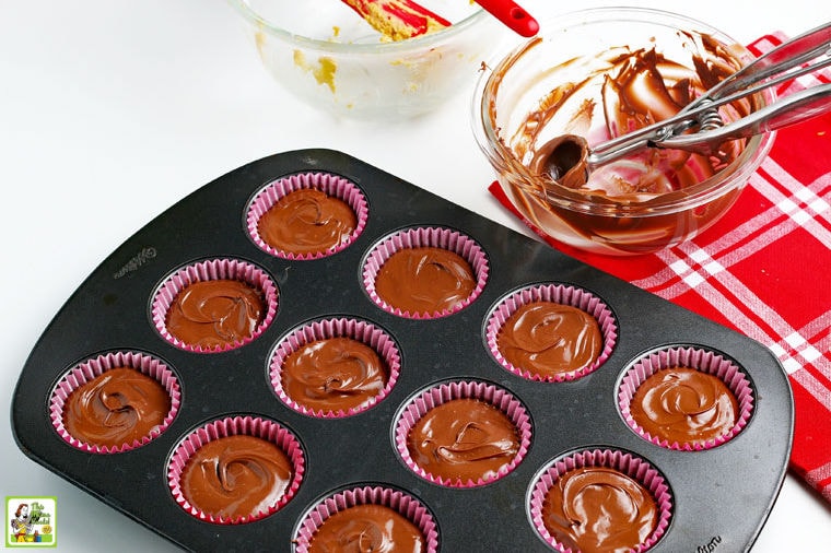 Adding the final layer of melted chocolate to the homemade peanut butter cups with empty bowls and a cookie scoop in the background.