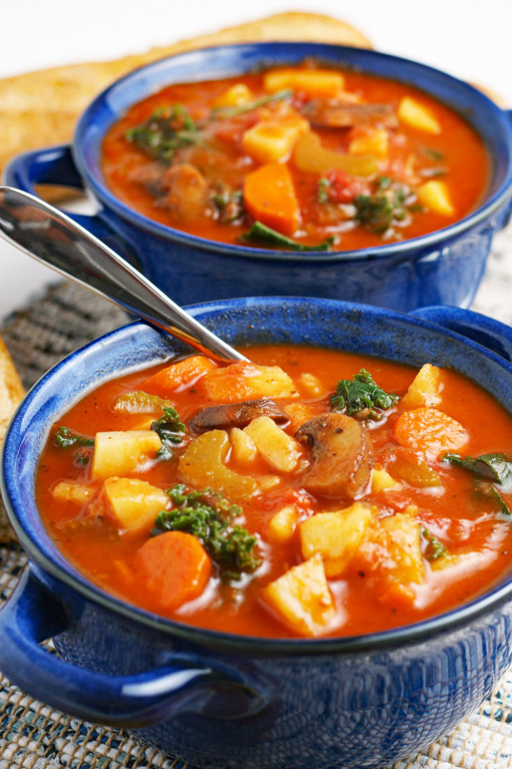 Close up of a blue bowls of vegetable soup with soup spoon.