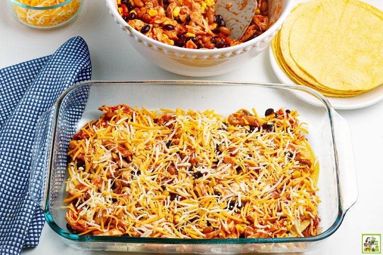 Layer of the chicken enchilada casserole with shredded cheese in a glass baking dish.