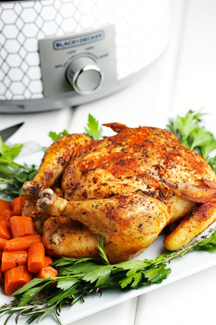 A slow cooker whole chicken on a platter with carrots and parsley.