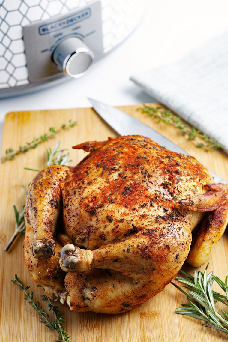 A roasted crockpot whole chicken on a wooden cutting board with a knife.
