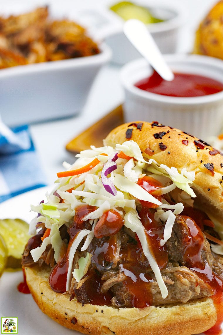 A BBQ pulled pork sandwich with coleslaw and pickles and a small jar of BBQ sauce.