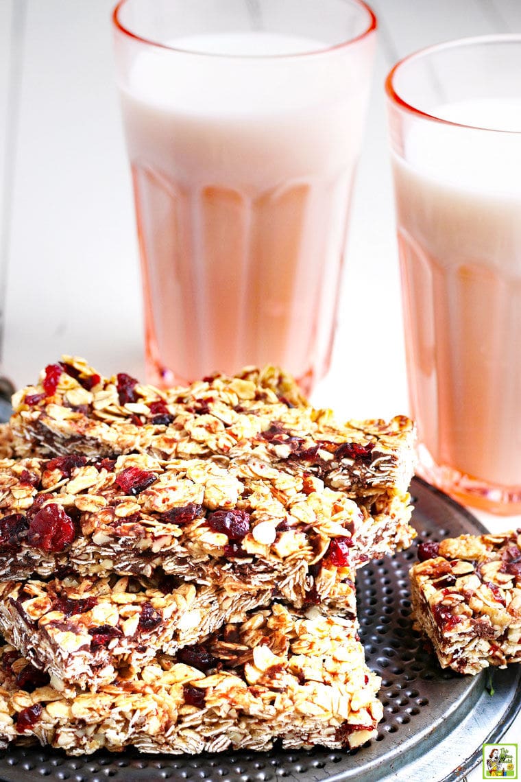 A stack of homemade granola bars on a plate placed on a metal trivet next to two pink glasses of milk.plate placed on a metal trivel next to two pink glasses of milk.