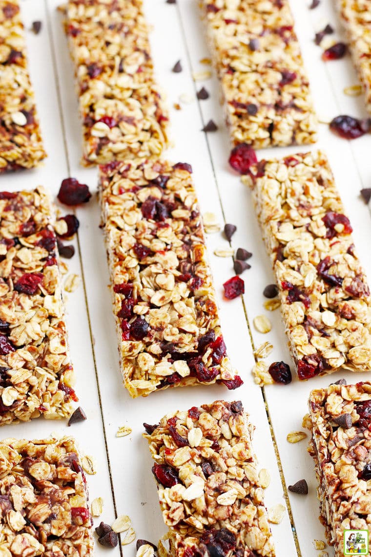Closeup of homemade granola bars made with old fashioned oats, mini chocolate chips, and dried cranberries on a white wooden board.