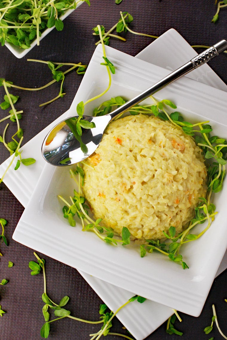 Overhead shot of seafood risotto served in a white bowl with a silver spoon garnished with pea greens.