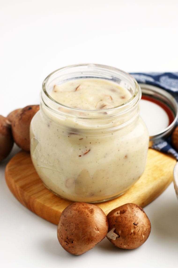 A mason jar of cream of mushroom soup on a wooden cutting board with mushrooms and a blue napkin.