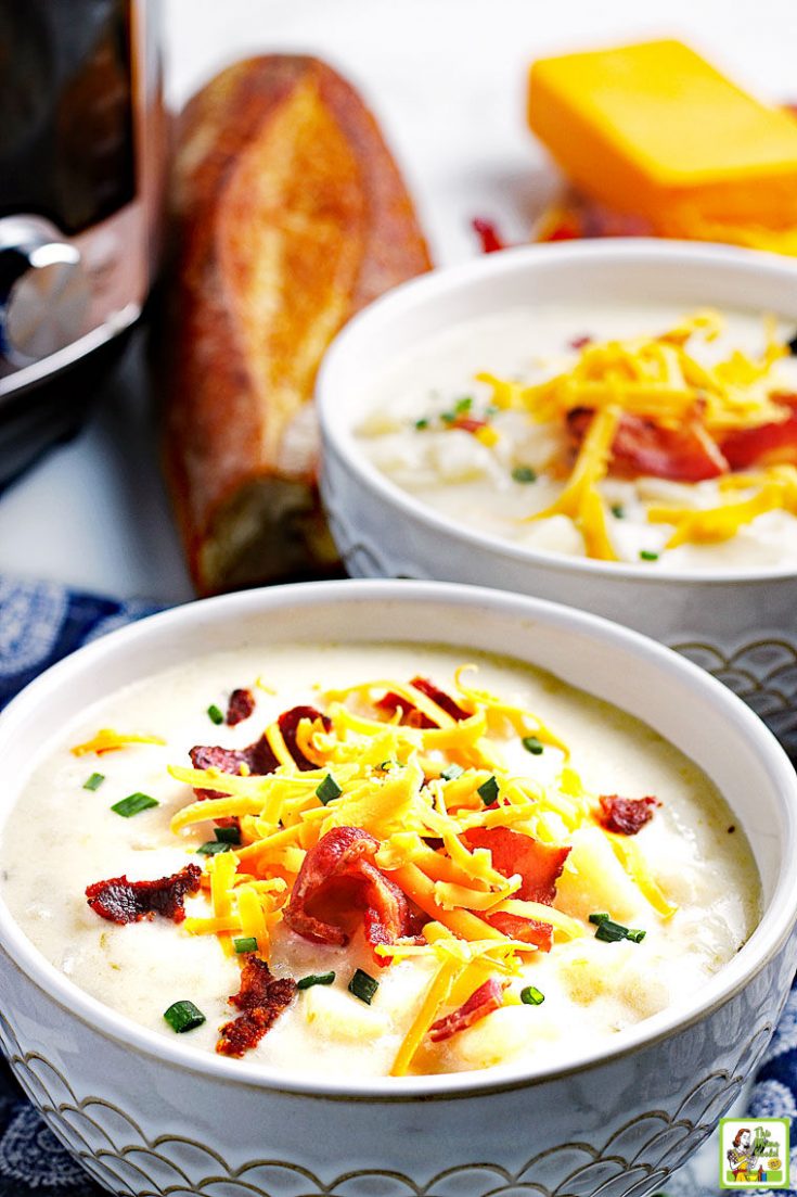 Bowls of Instant Pot Potato Soup topped with shredded cheese, bacon, and chives with bread, a block of cheese, and a pressure cooker in the background.