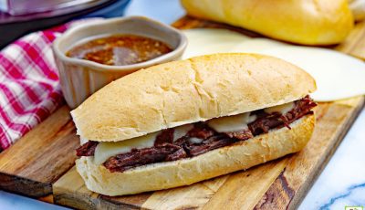 Instant Pot French Dip Sandwich with a bowl of au jus on a wooden cutting board with a napkin.