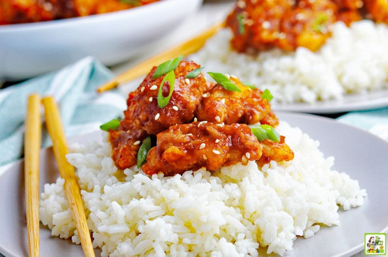 A plate of gluten free General Tso chicken served on rice with chopsticks.