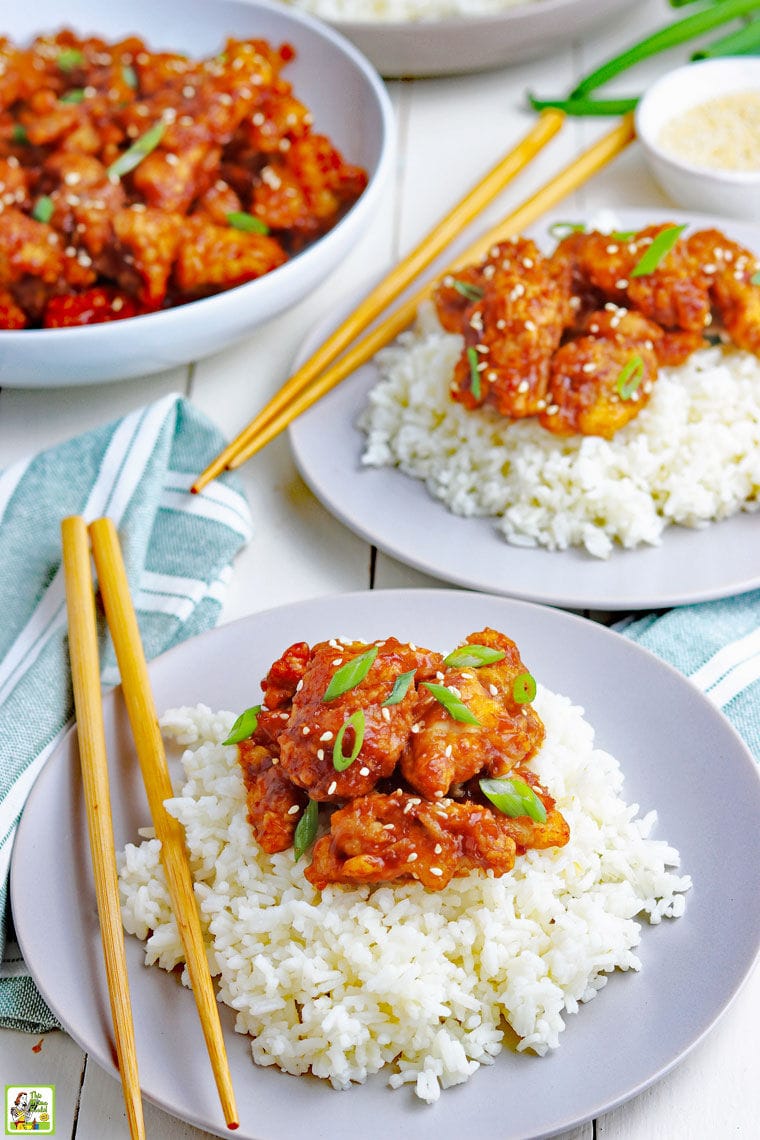 Plates of General Tso's chicken served on rice with chopsticks and a large bowl of cooked chicken in the background.