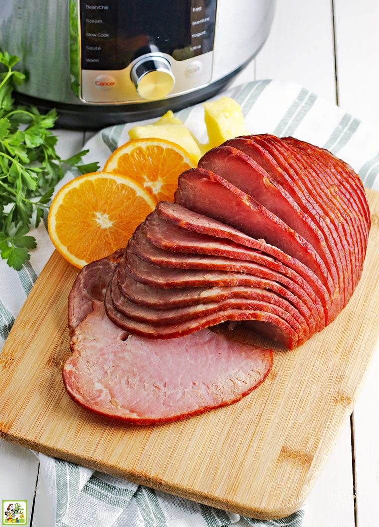 Spiral cut ham on a wooden cutting board with orange slices with an instant pot pressure cooker.