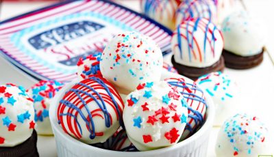 Red, white and blue Oreo balls in a bowl and with Oreos on a tabletop.
