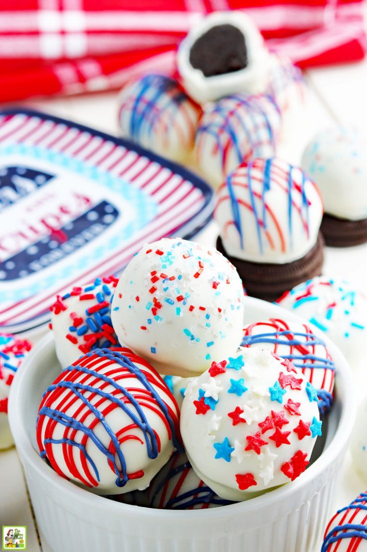 Red, white and blue Oreo balls in a bowl and with Oreos and holiday paperplates on a festive tabletop.