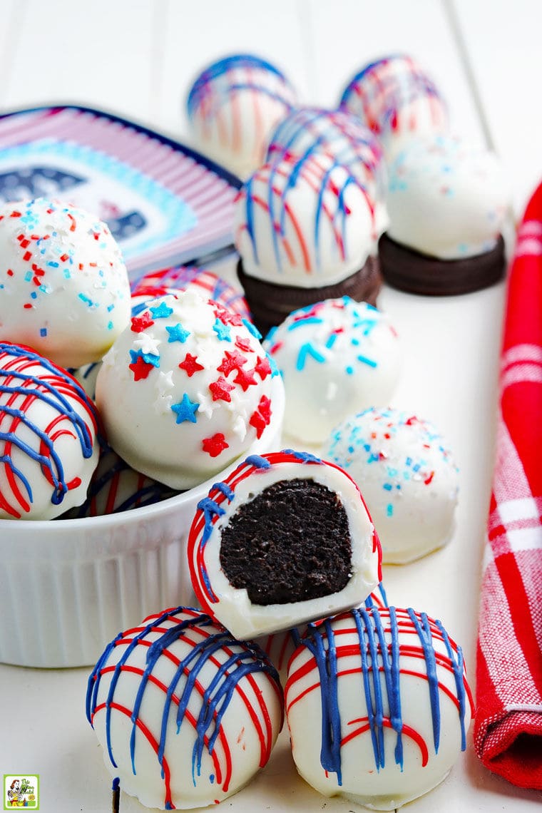 Festive striped red, white and blue Oreo cake balls in a bowl and on a white tabletop with a red cloth napkin.