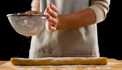 Woman sprinkling powdered sugar over baking dough.
