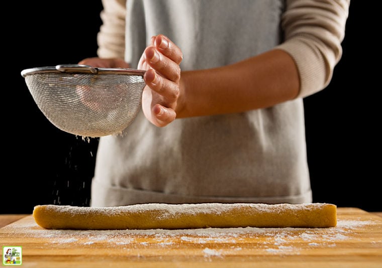 Woman sprinkling powdered sugar over baking dough.