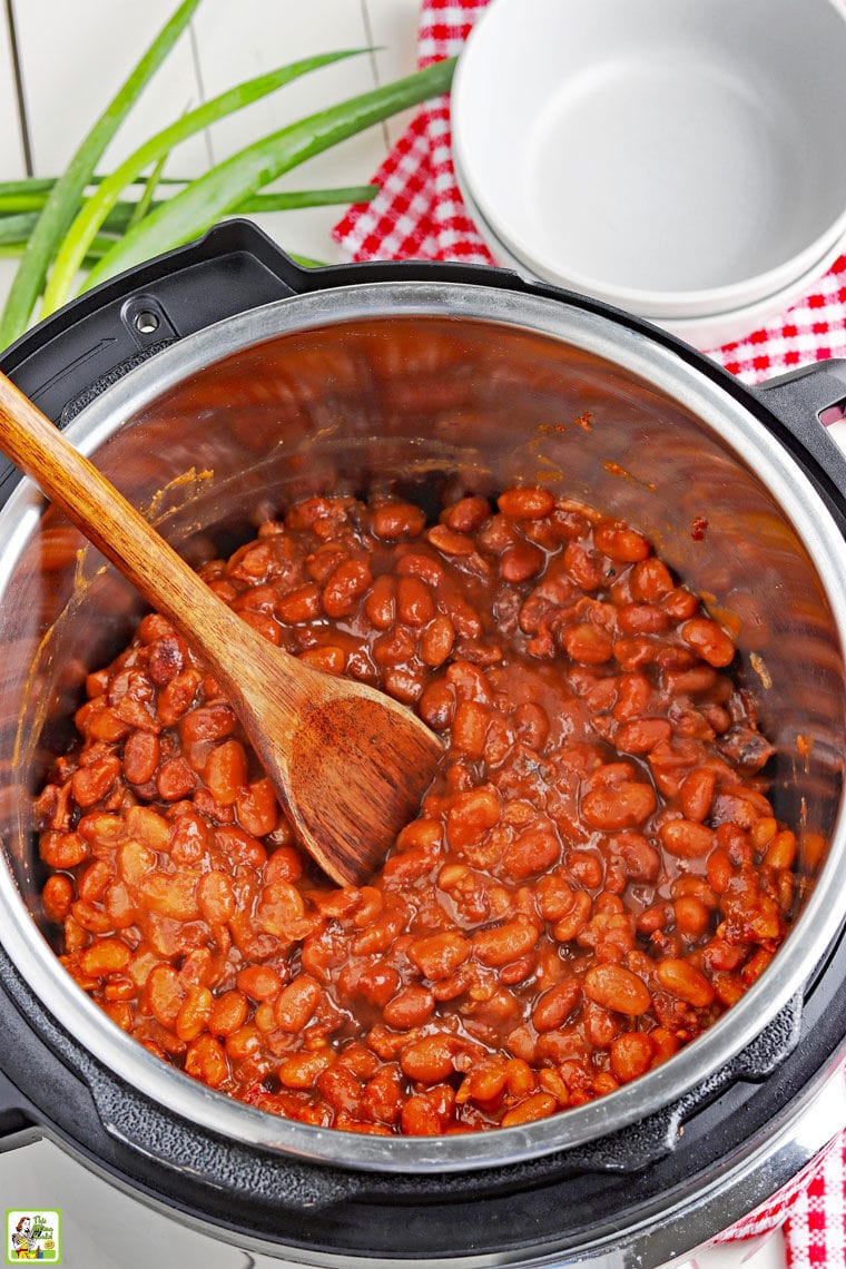 Overhead shot of a wooden spoon in a pot of pressure cooker baked beans with bowls and napkins.