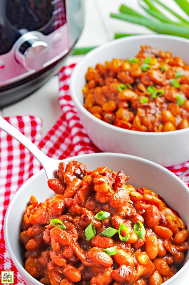 A fork dipped into bowls of baked beans with a pressure cooker in the background.