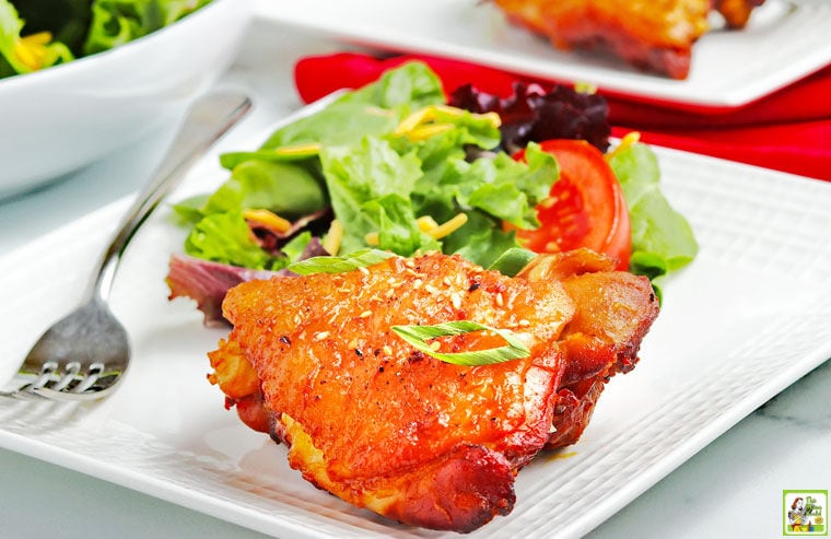 A piece of Instant Pot Chicken Thigh with Honey Garlic Sauce on a white plate with a fork, salad, and red napkin.