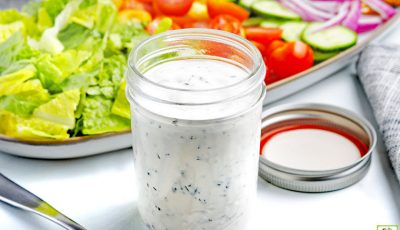 A mason jar of Low-Carb Keto Ranch Dressing with a platter of salad fixings.
