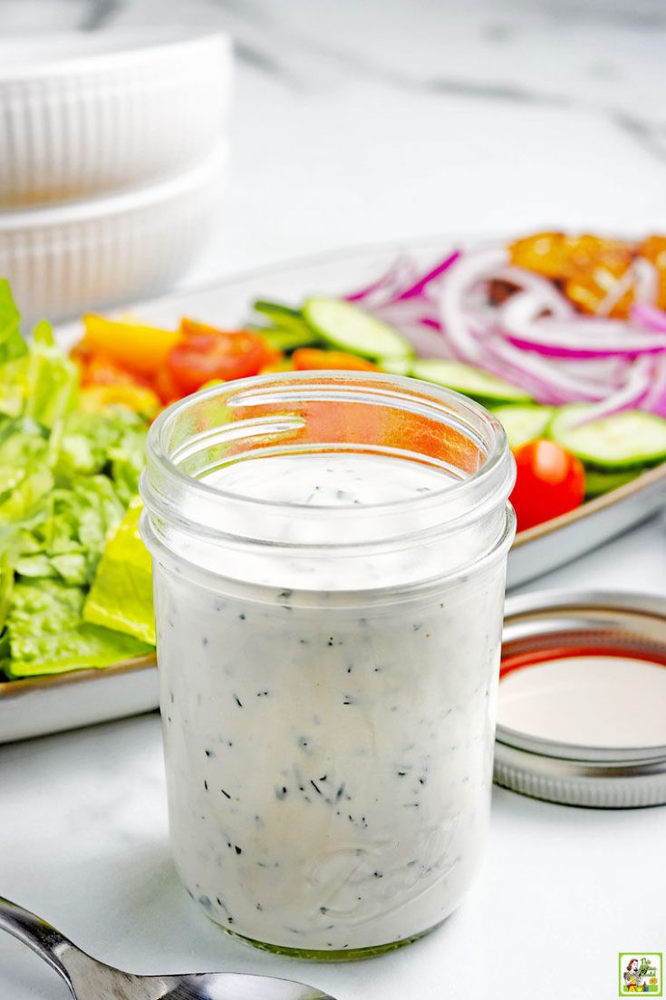 A mason jar of Low-Carb Keto Ranch Dressing with a platter of salad fixings, bowls, and a fork.