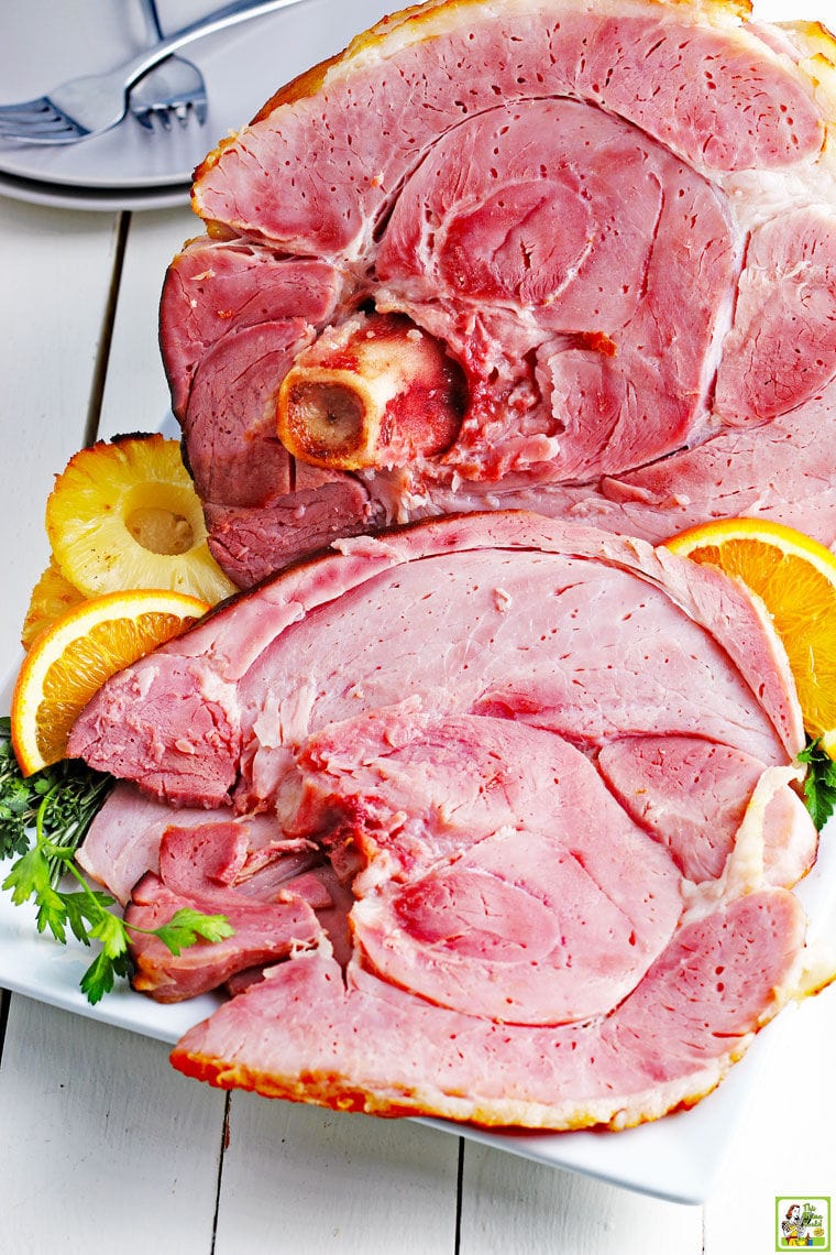 Slices of a spiral cut ham on a white platter with slices of oranges.