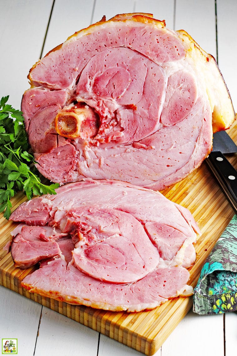 Slices of a spiral cut ham on a wooden platter with knife and green and blue napkins. 