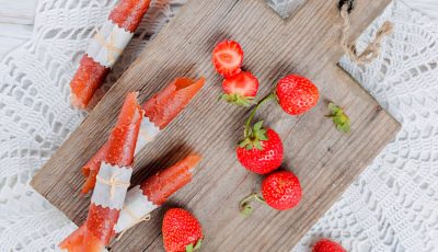 Strawberry Fruit Leather Roll-Ups on a wooden cutting board with strawberries.