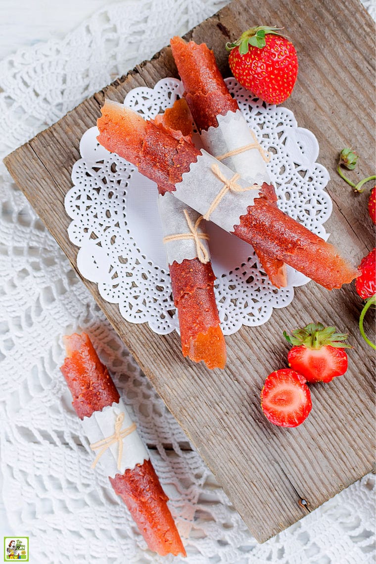 Strawberry Fruit Leather Roll-Ups on a lace doily on a wooden cutting board with strawberries.