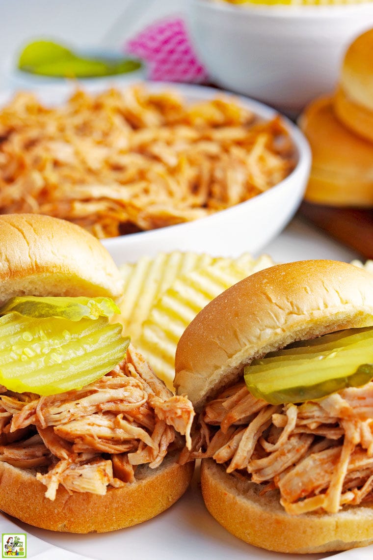 Closeup of shredded BBQ chicken sandwiches with pickles, potato chips, and a bowl of Instant Pot Pulled BBQ chicken.